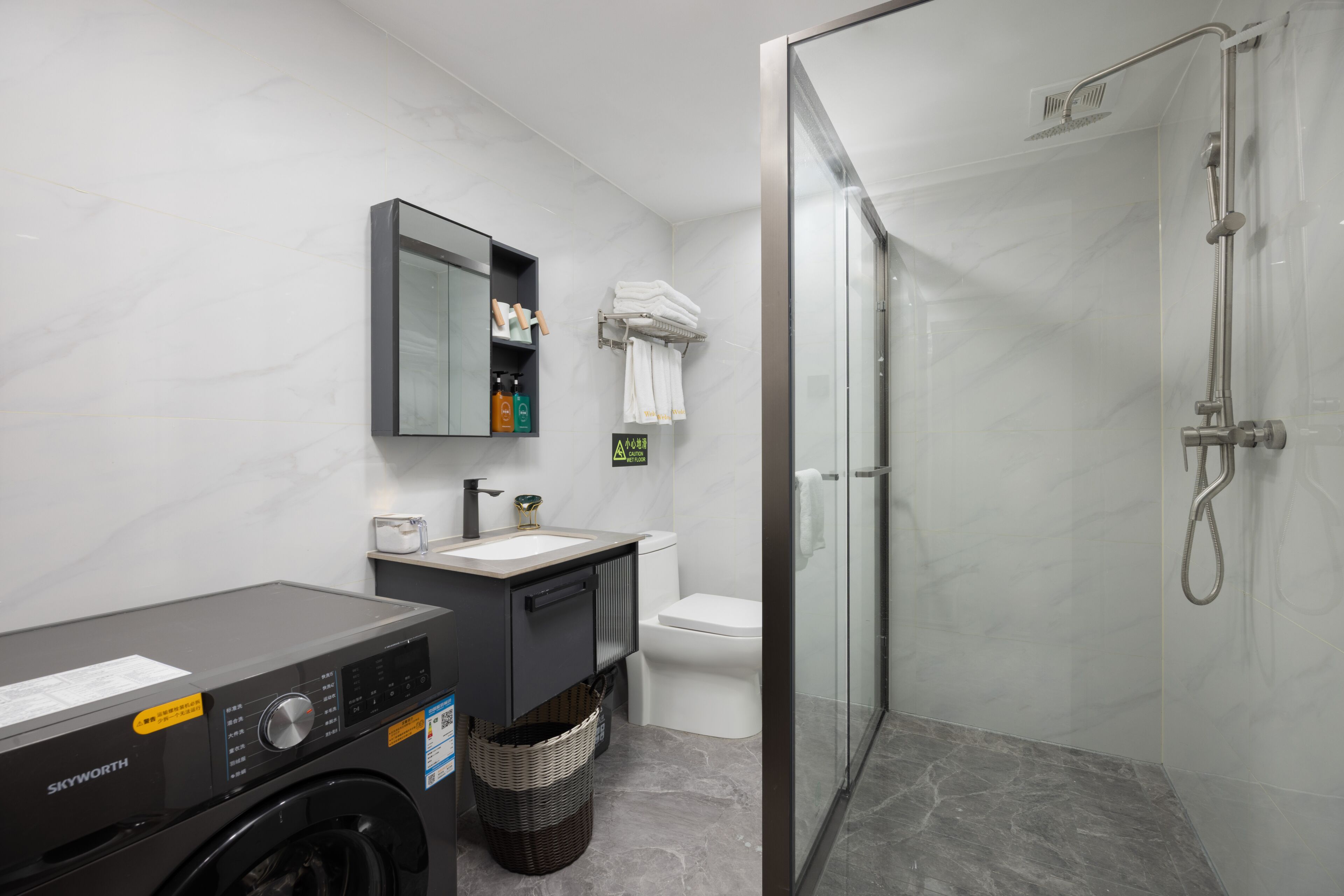 A modern bathroom with a washing machine, a sink, a toilet, and a glass-enclosed shower.