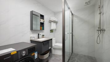 A modern bathroom with a washing machine, a sink, a toilet, and a glass-enclosed shower.