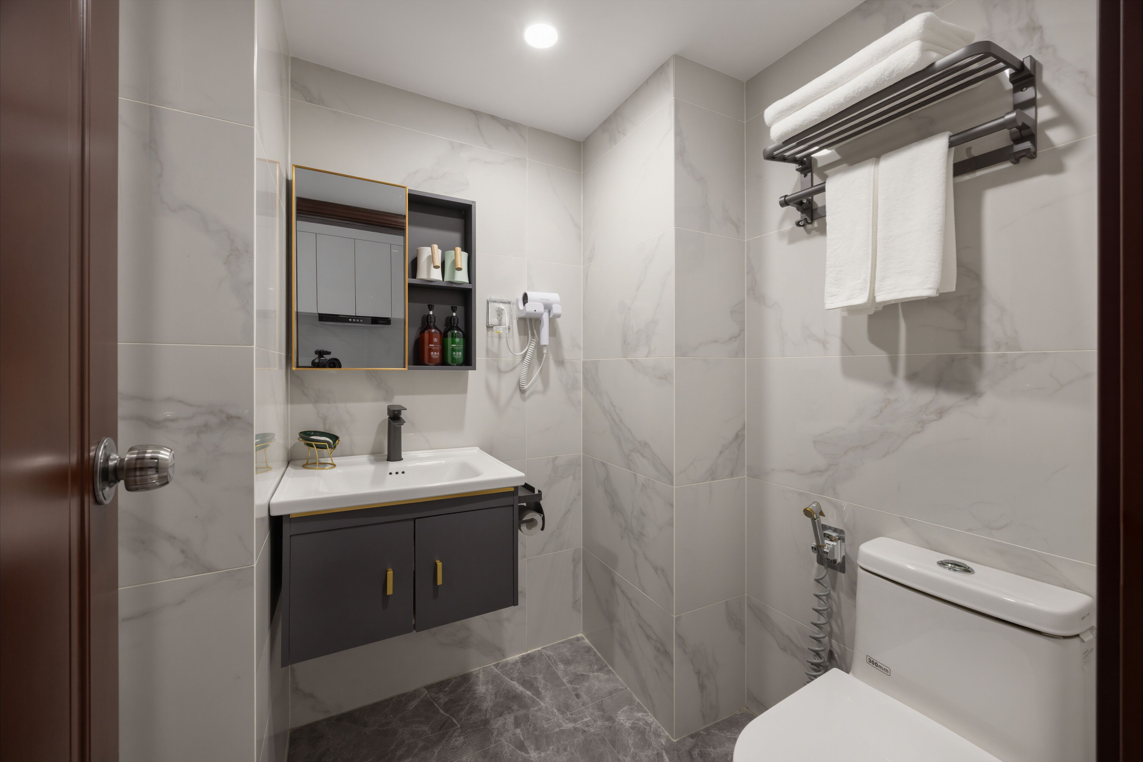 Un baño con lavamanos blanco, mueble oscuro y un inodoro.