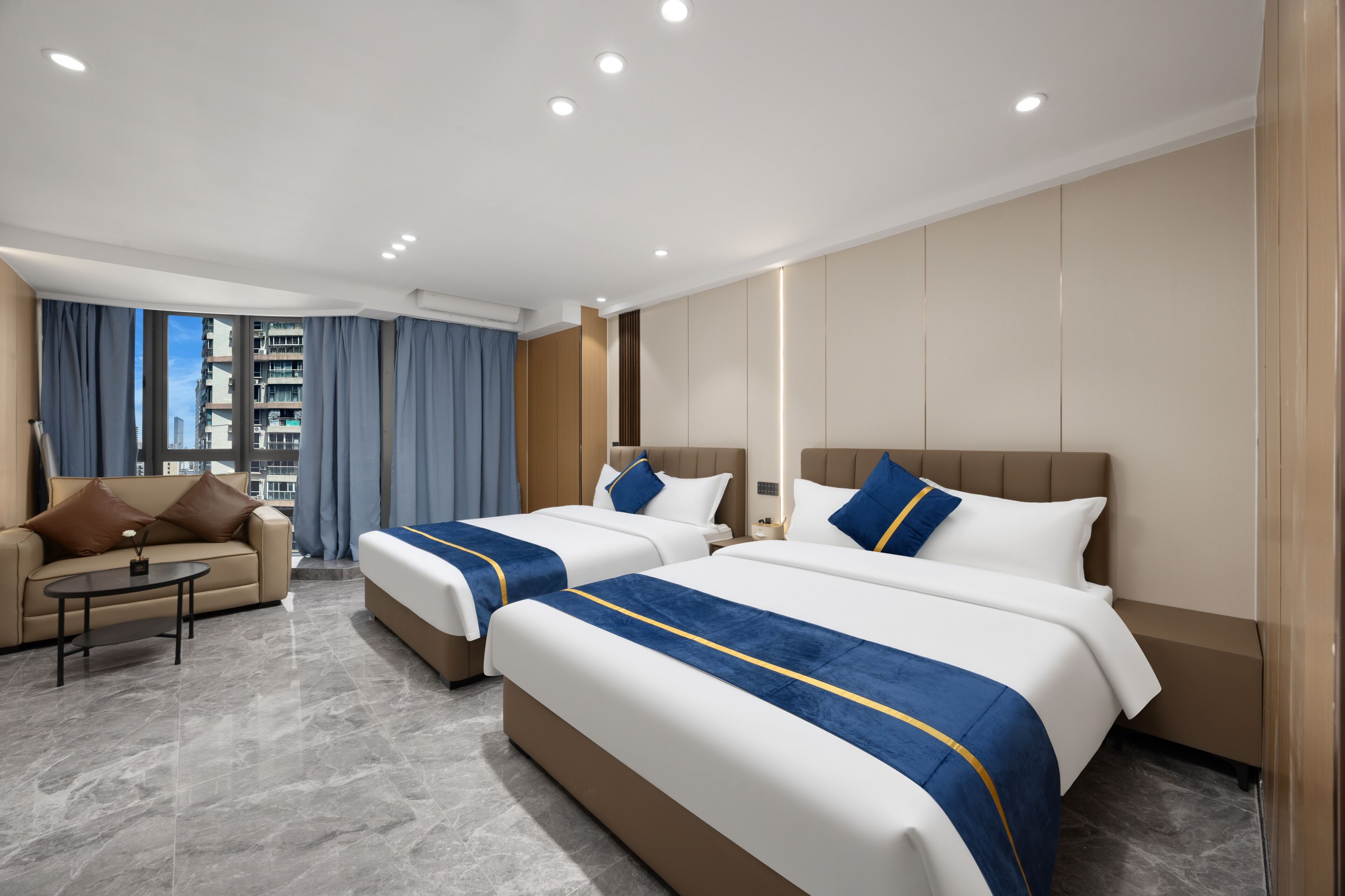 A hotel room with two beds, a sofa, a coffee table, and a view of the city.