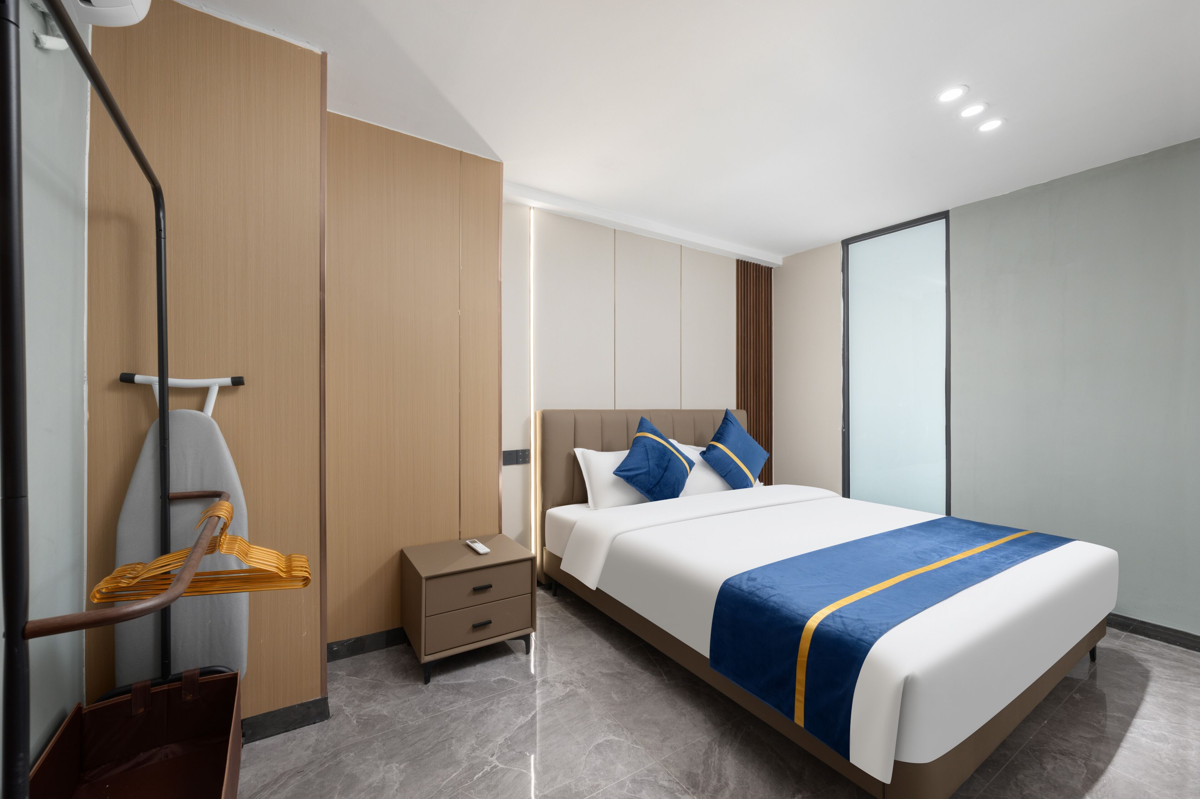A modern hotel room with a large bed, a bedside table, a wardrobe, and a mirror.