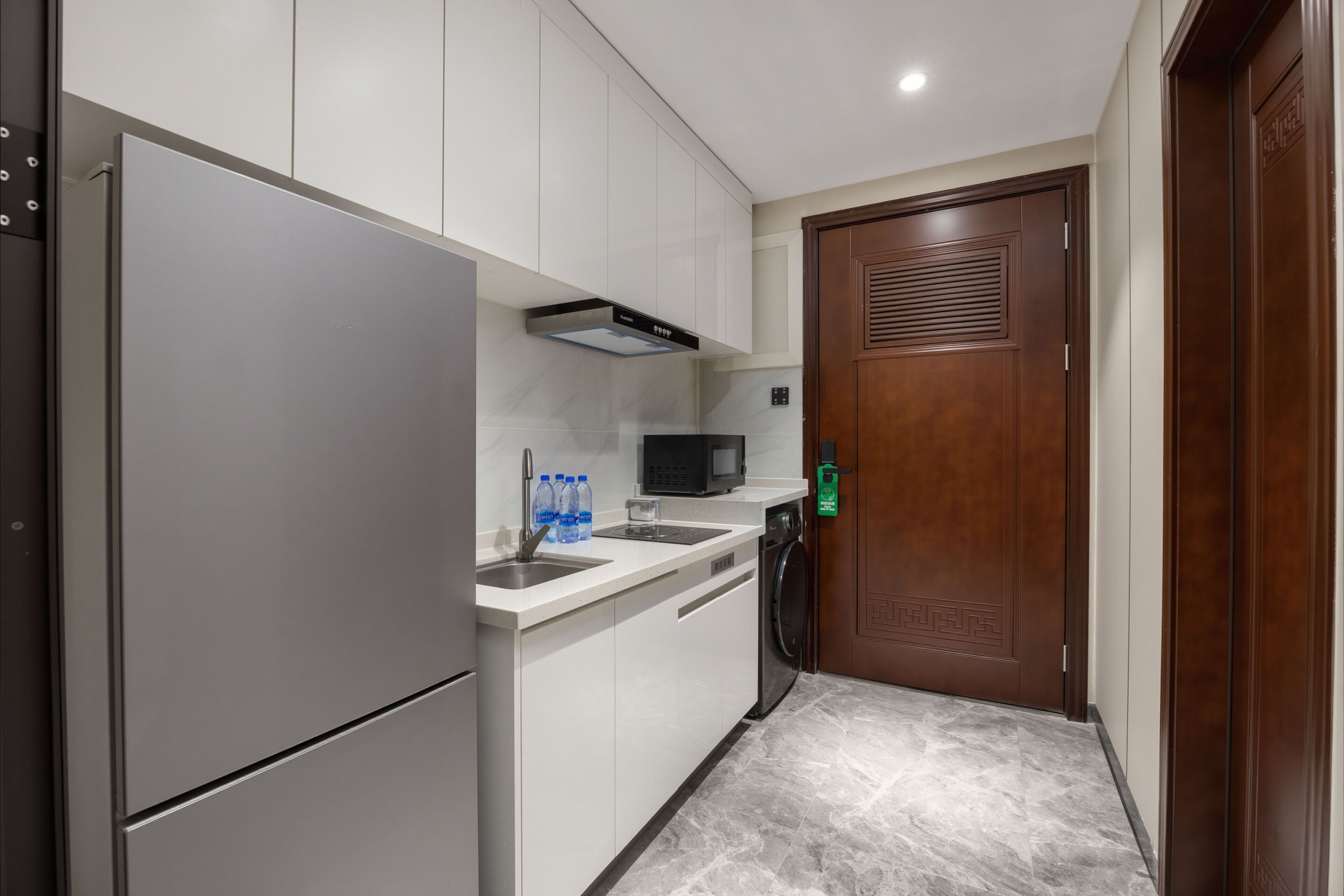 A compact kitchen with a refrigerator, microwave, sink, and a washing machine.