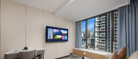 Habitación de hotel moderna con un televisor de pantalla plana montado en la pared, un área de comedor con mesa y sillas, una mesa de centro redonda y un sofá.