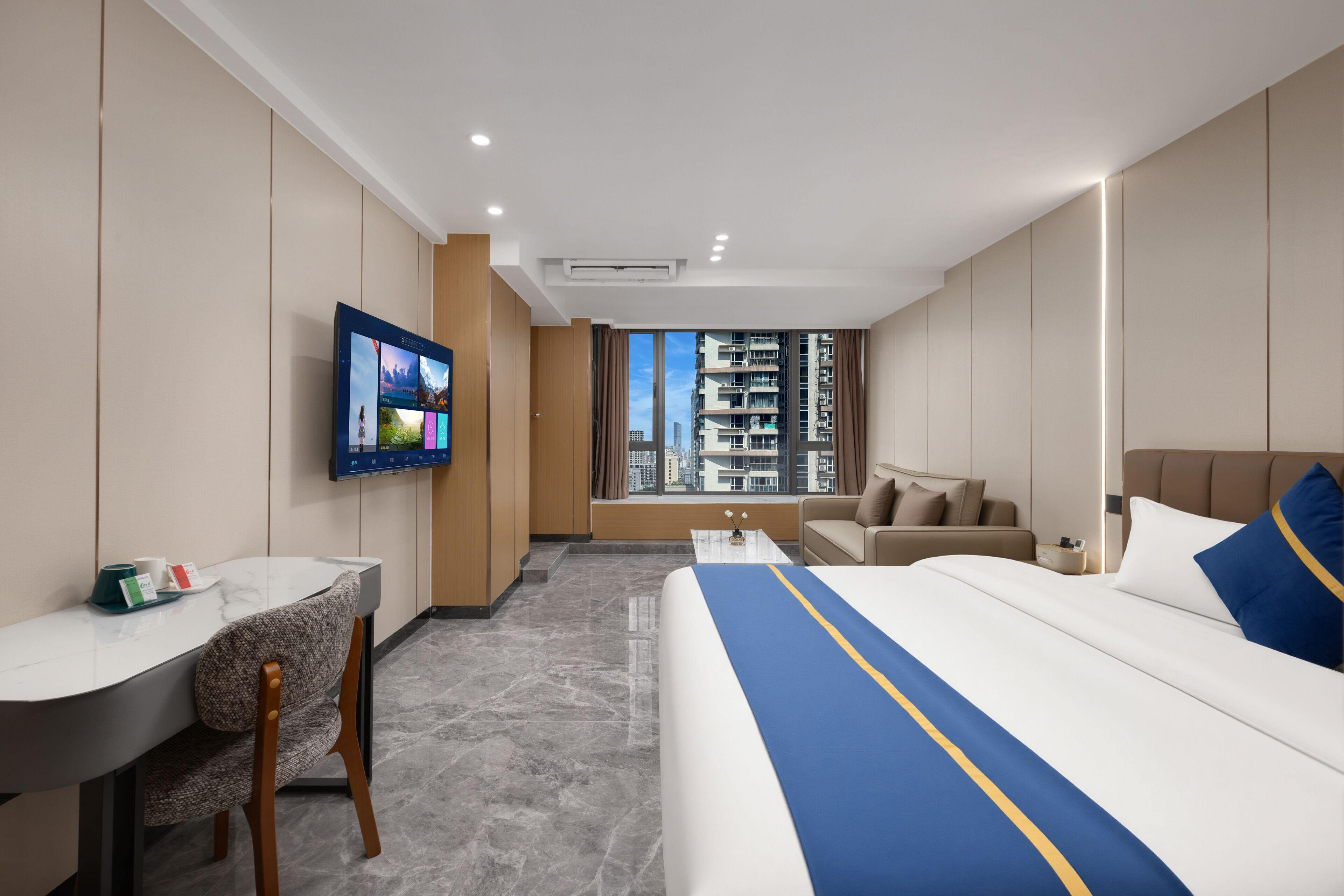 Habitación de hotel con cama, escritorio, silla, televisor y vistas a la ciudad.
