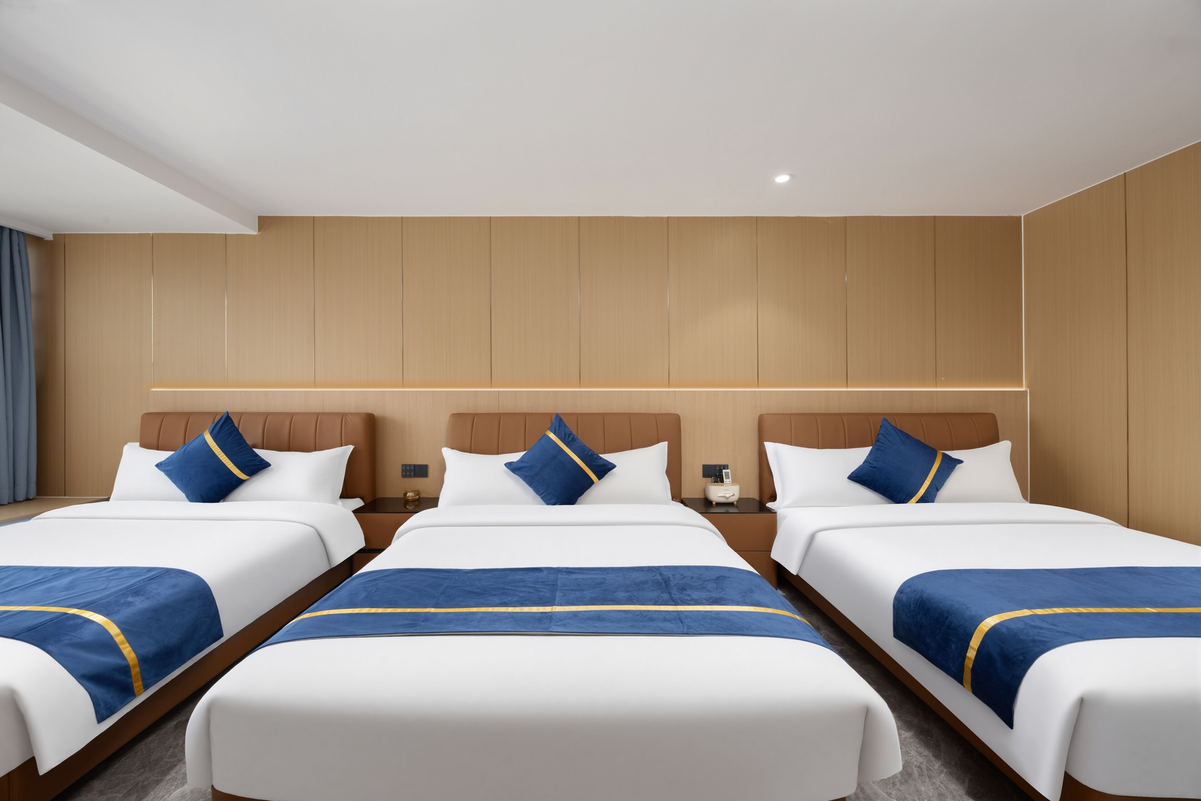 A hotel room with three beds, wooden panel walls, and a nightstand with a lamp.