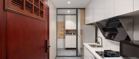 A modern kitchen with a built-in stove, a microwave, and a sink. There is a wooden door on the left and a pantry in the background.