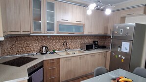 A compact kitchen with wooden cabinets, a microwave, a refrigerator, and a dining table with chairs.