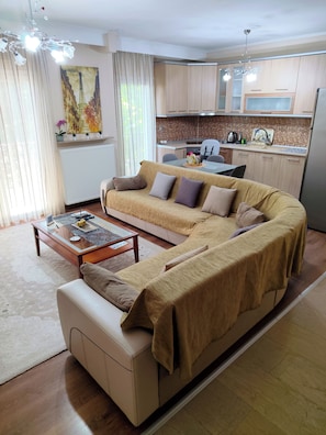 A living room with a sofa, coffee table, and a kitchen area in the background. - Cozy family apartment near the waterfalls of Edessa (Edessa)