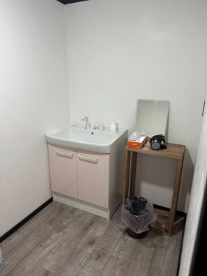 A bathroom with a white sink, a mirror, a wooden stool, and a trash bin.