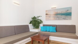 A modern living room with a sofa, a coffee table, a potted plant, and a painting of a beach scene. - Makai Bungalows (San Bartolomé de Tirajana)