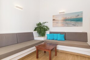 Una sala de estar moderna con un sofá, una mesa de centro, una planta en maceta y un cuadro de una playa.