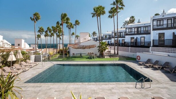 A pool area with lounge chairs, palm trees, and a view of the ocean. - Makai Bungalows (San Bartolomé de Tirajana)