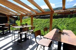 An outdoor patio with wooden tables and chairs, surrounded by greenery and a mountain view. - Rauris Penthouse with Fireplace (Rauris)