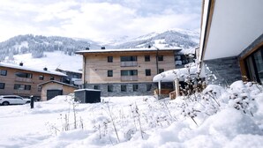 A modern building with a stone facade and multiple windows, surrounded by snow-covered ground and mountains in the background. - Rauris Penthouse with Fireplace (Rauris)