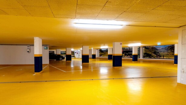 A parking garage with yellow floors and white pillars, featuring emergency exit signs and a fire extinguisher. - Rauris Penthouse with Fireplace (Rauris)