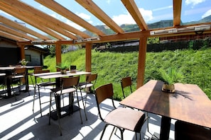 Eine Terrassengaststätte mit Holztischen und -stühlen, einer Pergola und Blick auf eine üppige, grüne Landschaft.