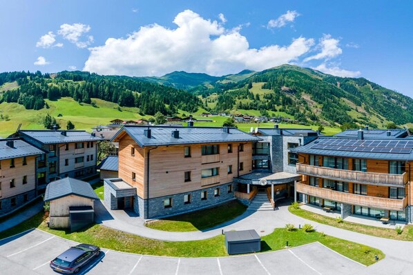 A modern building with multiple floors, a covered outdoor area, and a view of green hills in the background.