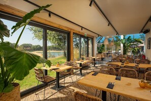 An outdoor dining area with wicker furniture, large windows, and a view of a lake. - Wilsumer Berge Resort - Hikers' Cabin (Wilsum)