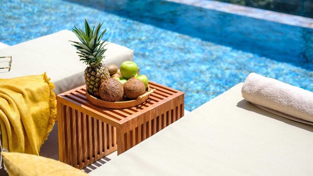 Et område ved poolen med en træblok, en ananas, kokosnødder og et håndklæde.