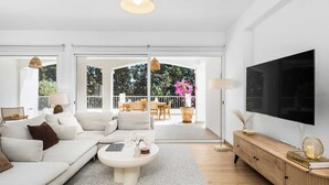 En moderne stue med sofa, sofabord, fjernsyn og en balkon med udendørs møbler.
