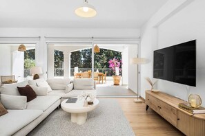 Ein modernes Wohnzimmer mit einer Couch, einem Couchtisch, einem Fernseher und einem Balkon mit Gartenmöbeln.