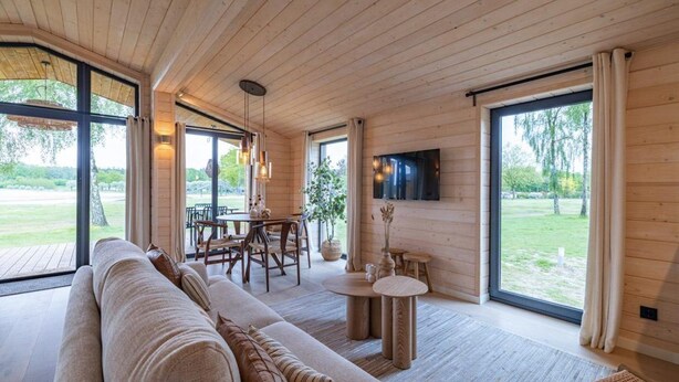 A modern interior with a wooden ceiling, large windows, a sofa, a dining table, and a TV mounted on the wall.
