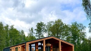 A modern wooden cabin with a covered porch, large windows, and a grassy yard.
