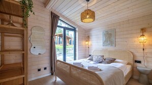 A wooden cabin bedroom with a bed, bedside lamps, a hanging light fixture, and a window with curtains.