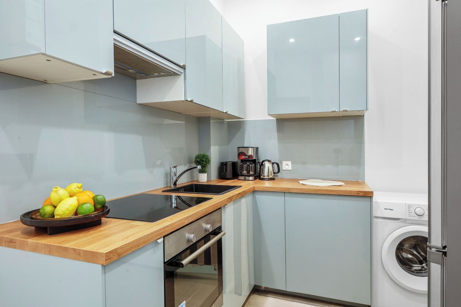 A compact kitchen with a sink, coffee maker, and a washing machine.