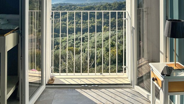 Un balcone aperto con vista su un paesaggio boschivo e colline lontane.