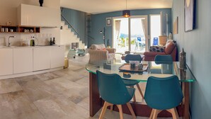 Una cucina moderna con un tavolo da pranzo in vetro, sedie color petrolio e una scala che conduce a un balcone.