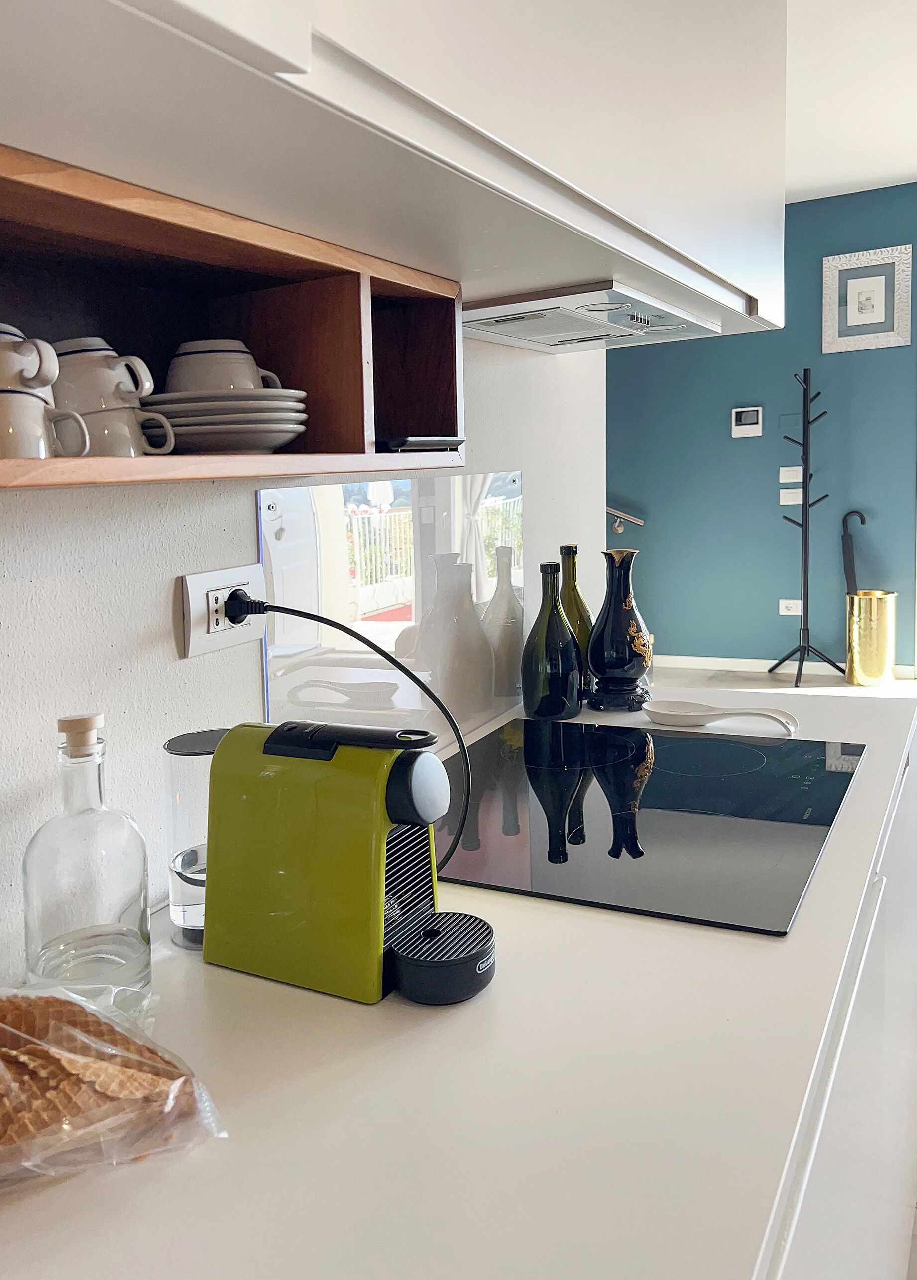 A modern kitchen with white cabinets, a built-in oven, and a countertop with a coffee maker, a kettle, and a bag of bread.