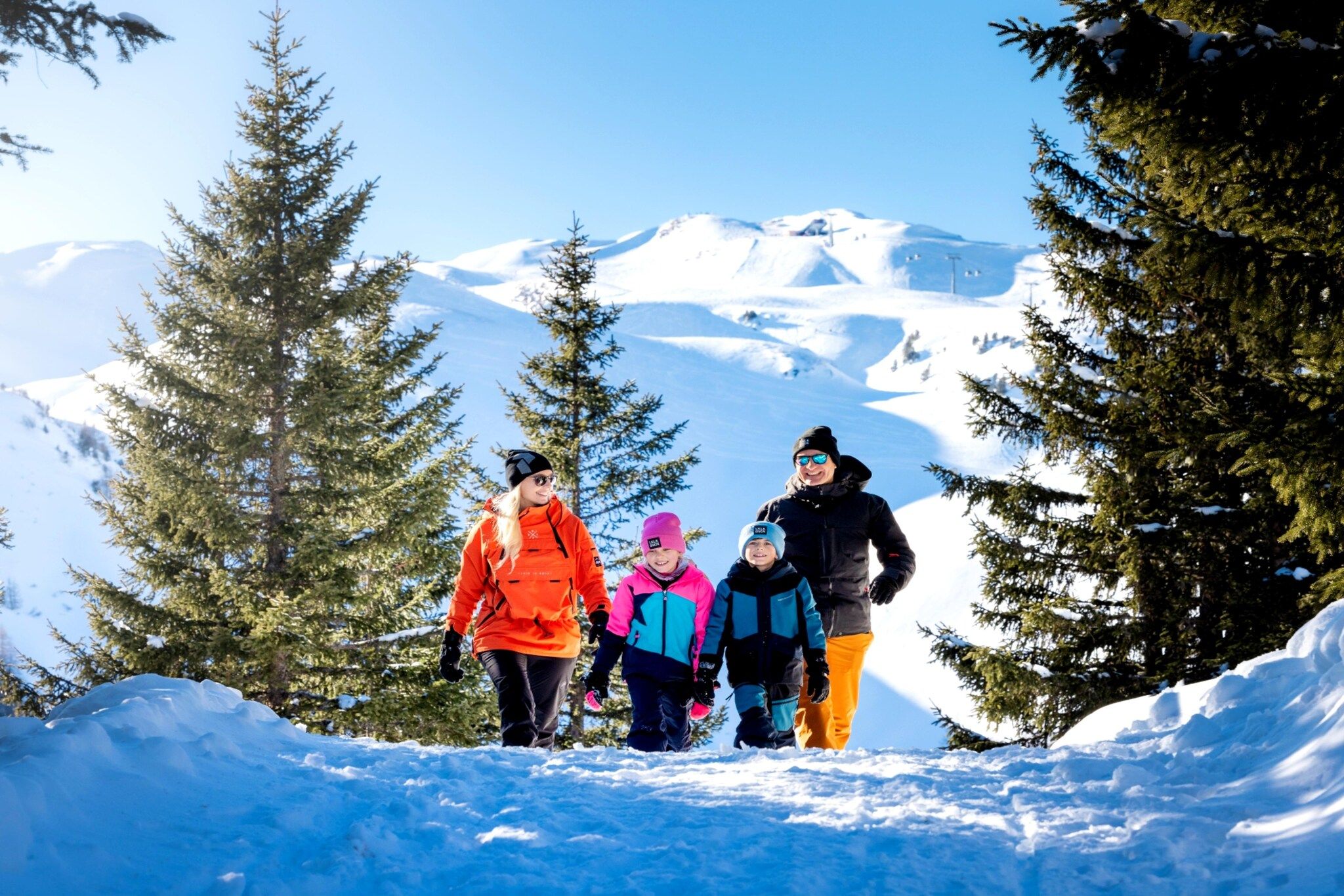 A group of people walking on a snowy path surrounded by trees and snow-covered mountains.