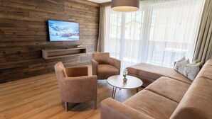 En moderne stue med trævæg, et fladskærms-tv, en sofa, to lænestole og et lille rundt bord.
