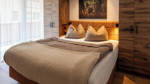 Et moderne soveværelse med sengegavl i træ, en stor seng med beige sengetøj og udsigt til en balkon.