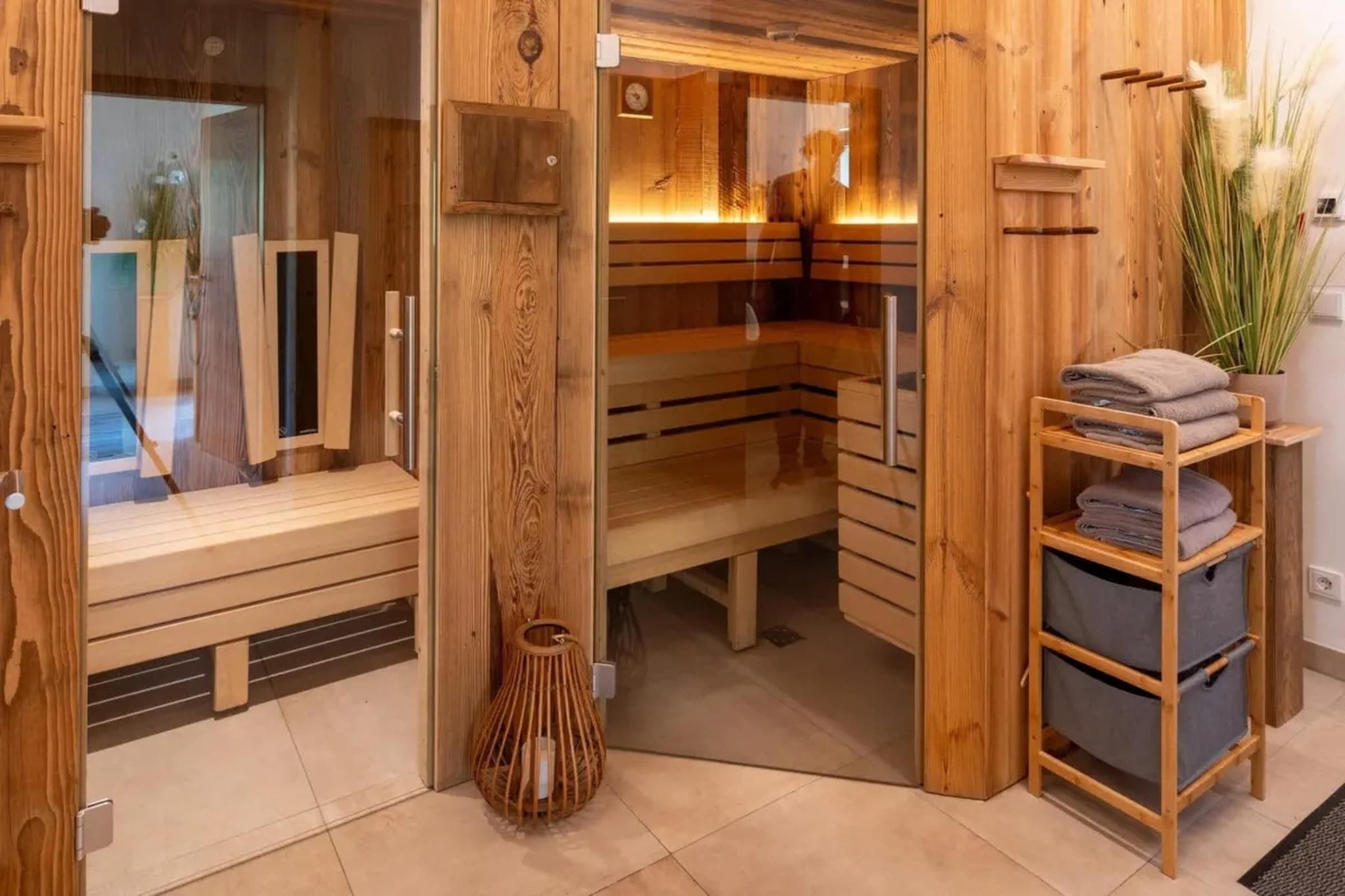 A wooden sauna room with benches, a glass door, and a shelf with towels.