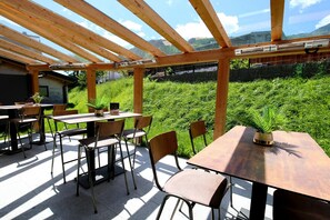 Eine Terrasse im Freien mit Holztischen und -stühlen, einer Pergola und Blick auf eine grüne Landschaft.