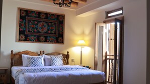 A bedroom with a wooden bed, a patterned rug, a chandelier, and a wall tapestry. - BAKOVUL HERITAGE  (Bukhara)