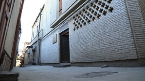 A narrow alleyway with a white brick building, a dark door, and a manhole cover. - BAKOVUL HERITAGE  (Bukhara)