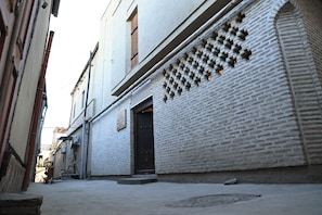 A narrow alleyway with a white brick building, a dark door, and a manhole cover. - BAKOVUL HERITAGE  (Bukhara)