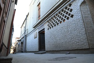 Un callejón estrecho con un edificio de ladrillo blanco, una puerta oscura y una tapa de alcantarilla.