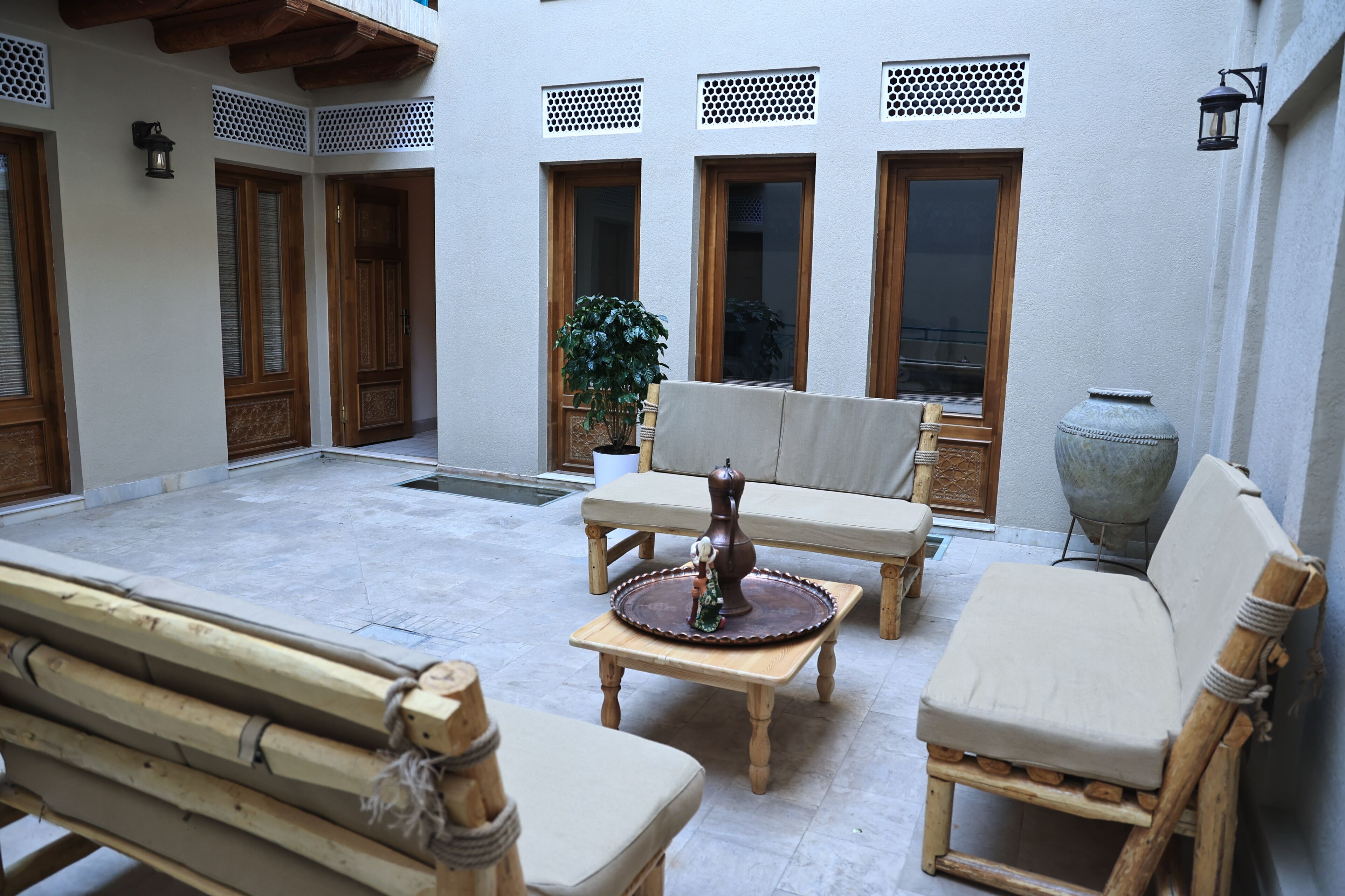 Un patio con un banco de madera, una mesa con un objeto decorativo, una silla acolchada y un jarrón grande.
