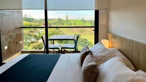 A hotel room with a bed, a view of a green landscape, and a small table and chair outside the window. - Rioverde Living suites- Apartahotel (Antioquia)