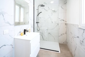 Un baño con ducha de mármol blanco, lavabo blanco con espejo y suelo color beige.