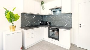 A compact kitchen with white cabinets, a black marble backsplash, a built-in oven, and a small refrigerator.