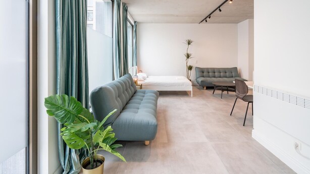 Una sala de estar moderna con un sofá, una cama, una mesa de comedor y un ventanal con cortinas.