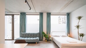 Un dormitorio moderno con sofá, cama, mesita de noche con lámpara y planta en maceta.