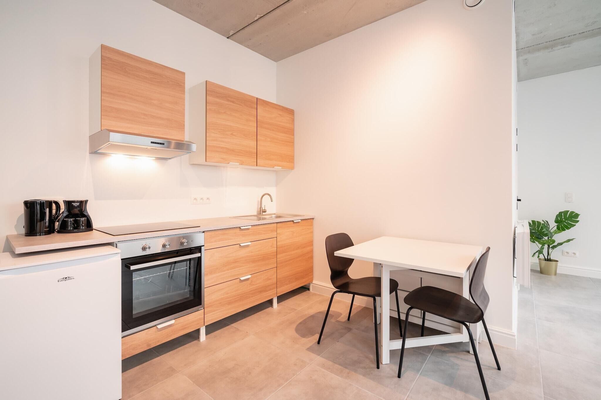Een moderne keuken met een wit aanrecht, roestvrijstalen apparatuur, houten kastjes en een eethoek met een witte tafel en zwarte stoelen.