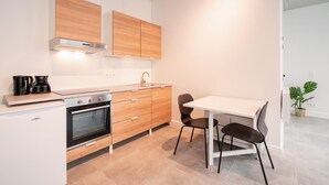 Una cocina moderna con encimera blanca, electrodomésticos de acero inoxidable, armarios de madera y un comedor con mesa blanca y sillas negras.