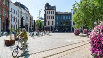 A person riding a bicycle on a paved area with tram tracks, surrounded by buildings with distinct architectural styles.
